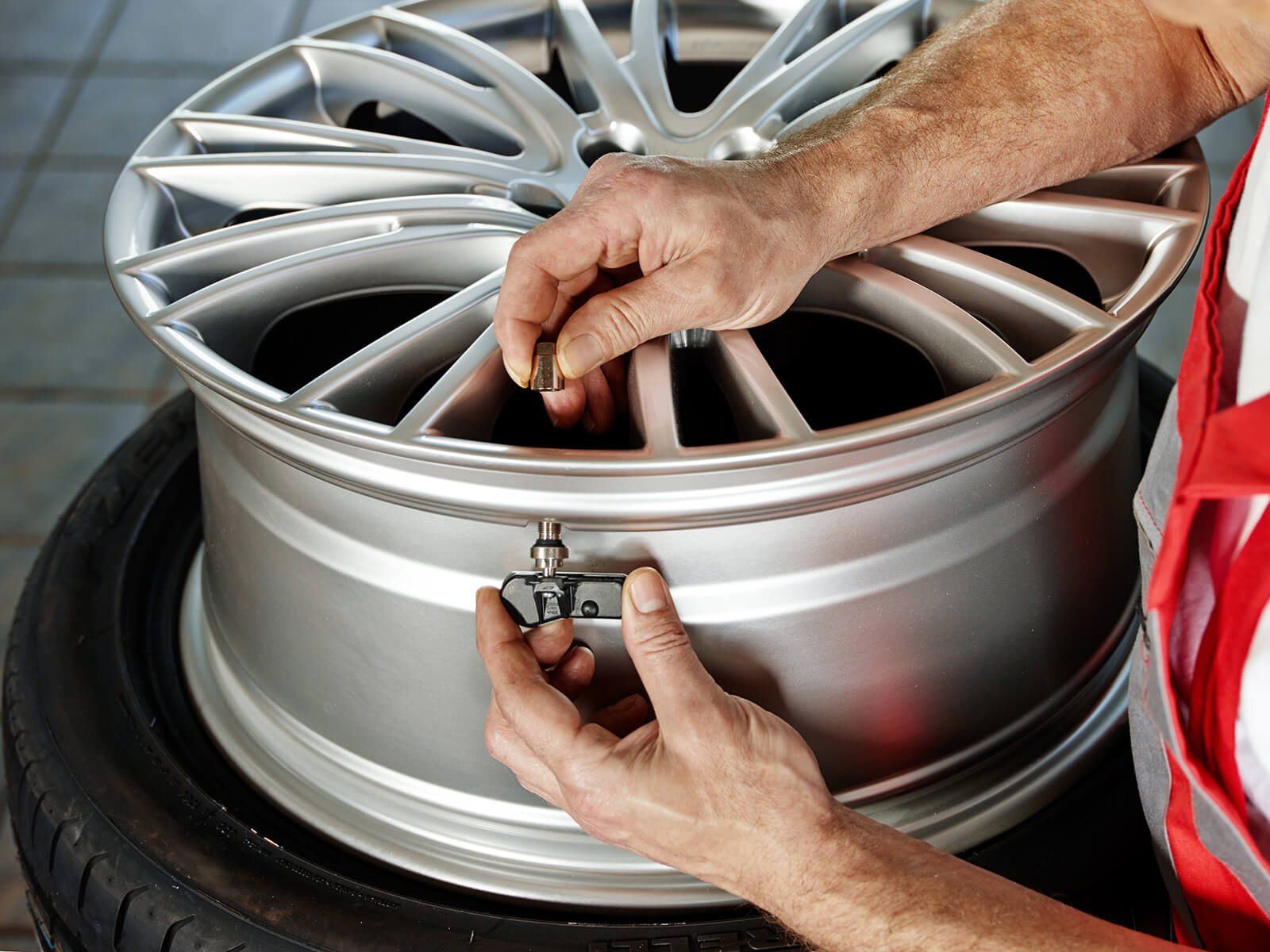 Mechanic fits tire pressure monitoring system attached to the wheel